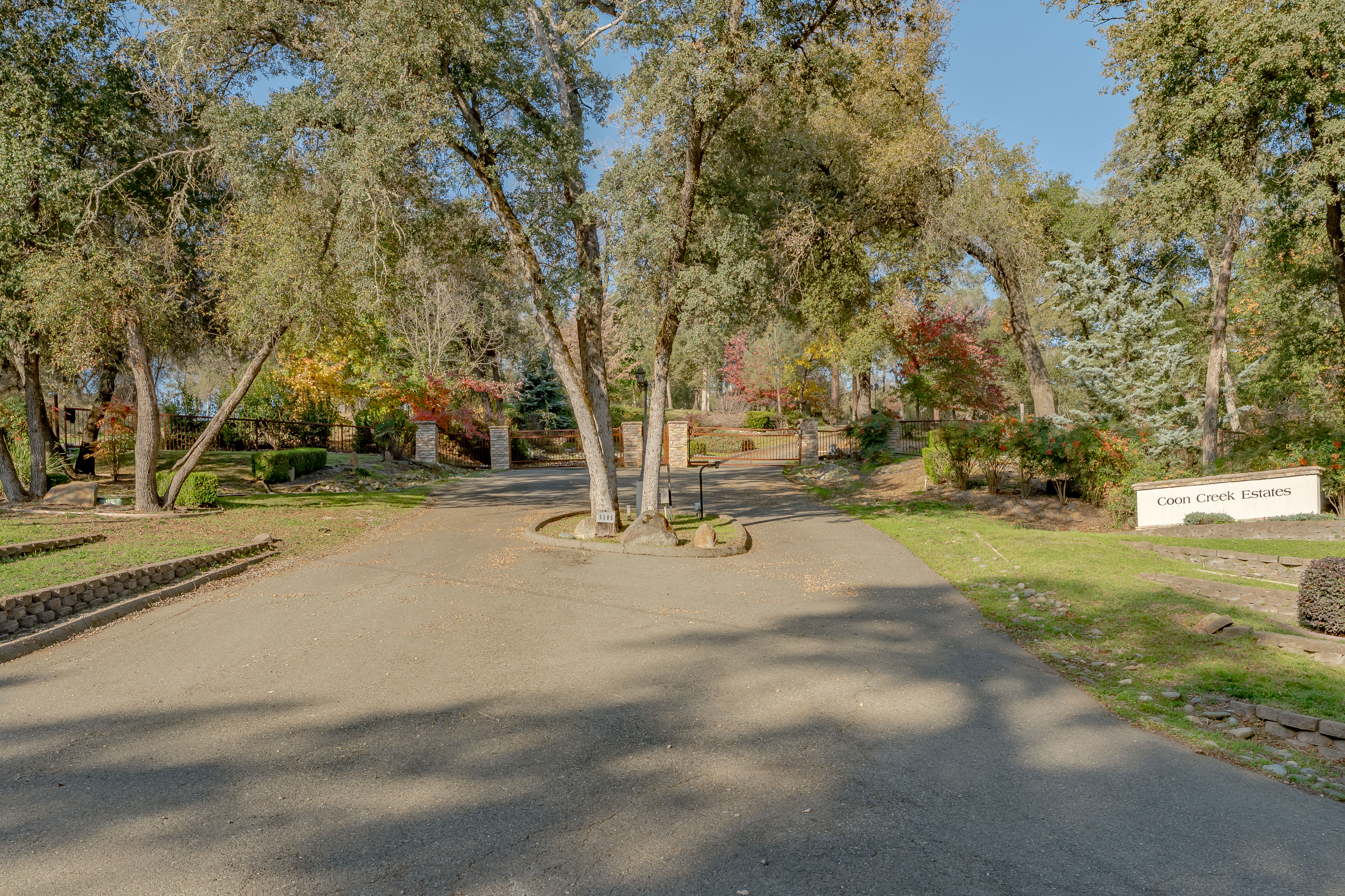 A winding road leading into a gated community surrounded by trees with colorful foliage, featuring a sign that reads 'Coon Creek Estates'.